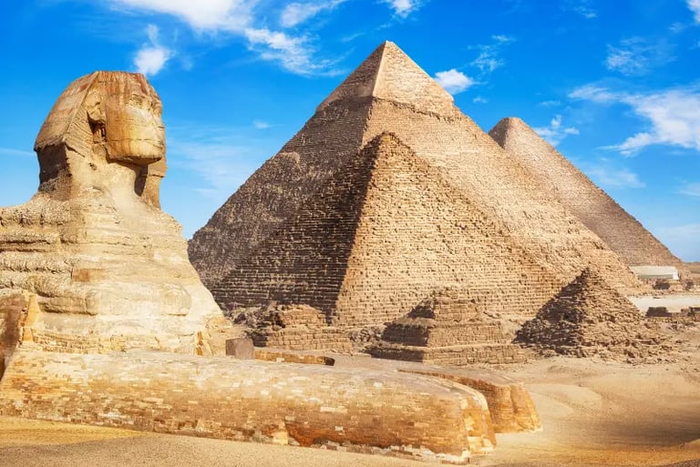 The Great Sphinx of Giza sitting in front of the ancient Egyptian pyramids under a clear blue sky.