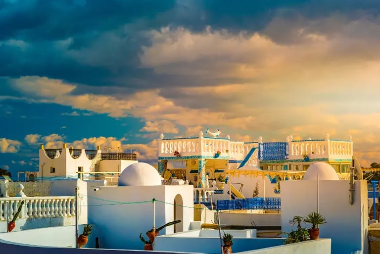 White domed houses in Sidi Bou Said, Tunisia under a dramatic sunset sky with golden clouds.