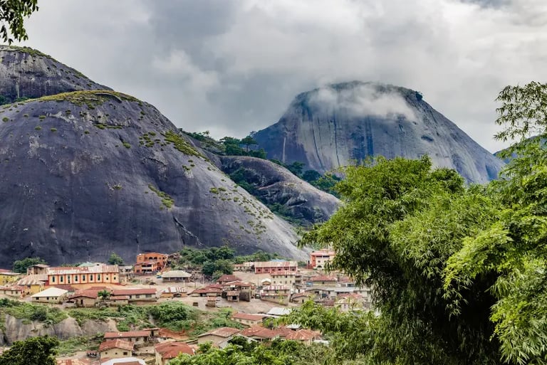A scenic view of Idanre Hills in Nigeria featuring a local village nestled beneath massive granite rock formations.