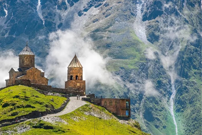 Gergeti Trinity Church stands on a lush green hill against the misty Caucasus Mountains in Georgia.