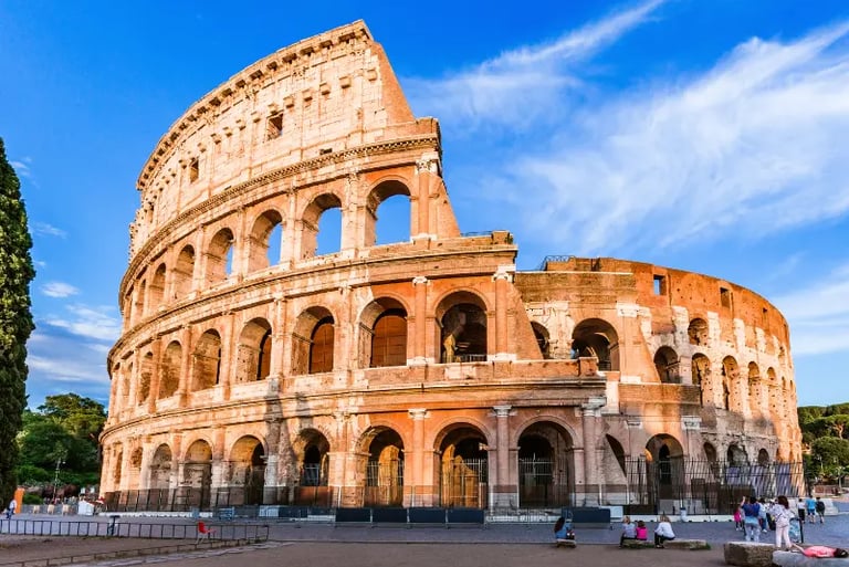 The Roman Colosseum in Italy, a historic stone amphitheater under a bright blue sky at sunset.
