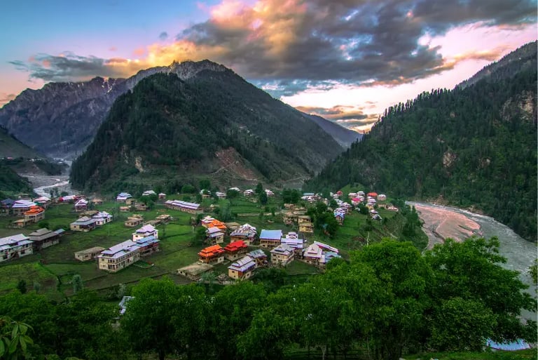 Scenic mountain village nestled in a lush green valley with a river flowing under a sunset sky.