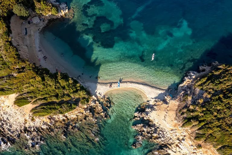 Aerial view of a secluded Greek island beach with crystal clear turquoise water and rocky coastline.