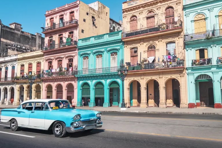 Vintage blue classic car taxi driving past colorful colonial buildings in Havana, Cuba.