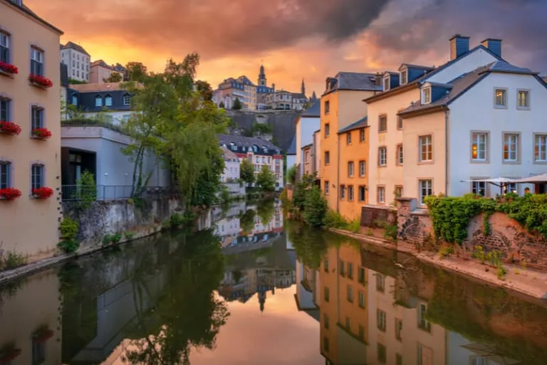 Historic buildings in Luxembourg City's Grund district reflected in the Alzette River at sunset.