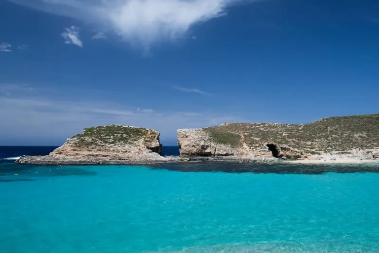 Turquoise waters of the Blue Lagoon in Comino, Malta, with limestone cliffs under a blue sky.