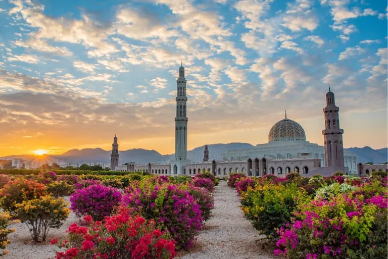 Sultan Qaboos Grand Mosque in Muscat, Oman at sunset with colorful garden flowers in the foreground.