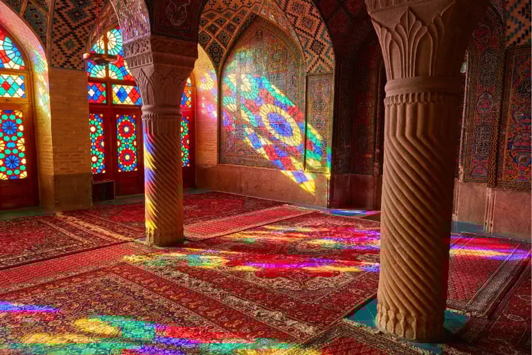 Stained glass light reflects colorful patterns on Persian rugs and carved pillars inside Nasir al-Mulk Mosque.