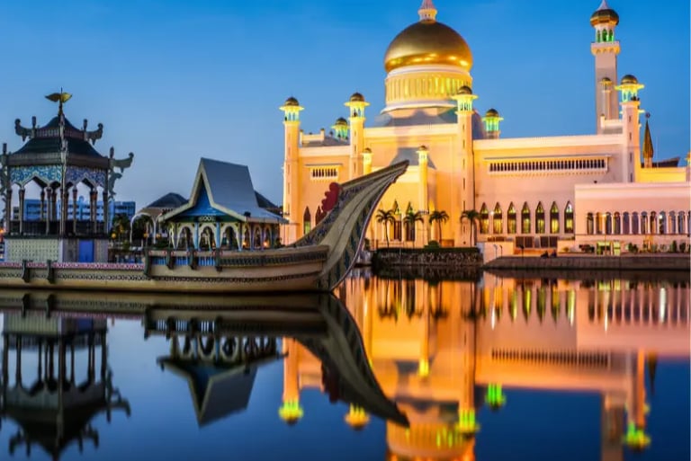 The Sultan Omar Ali Saifuddien Mosque in Brunei at dusk with a ceremonial stone boat reflected in the water.
