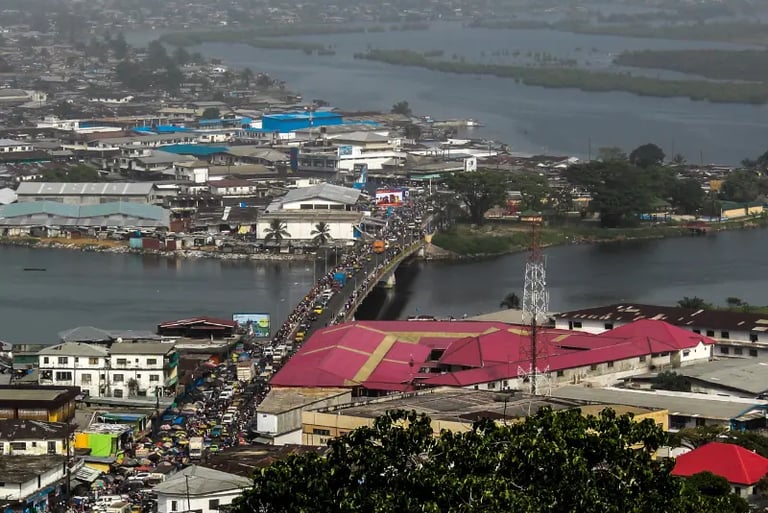 Aerial view of a busy bridge with heavy traffic crossing a river in a densely populated African city.
