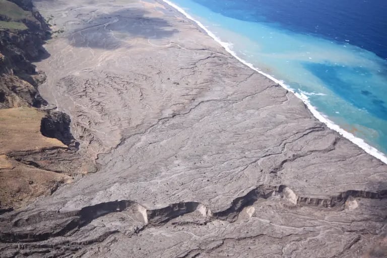 Aerial view of a volcanic landscape with black sand beach meeting turquoise ocean water.