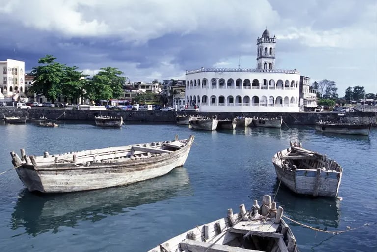 Traditional wooden dhow boats floating in the harbor of Moroni, Comoros, near a white domed mosque.