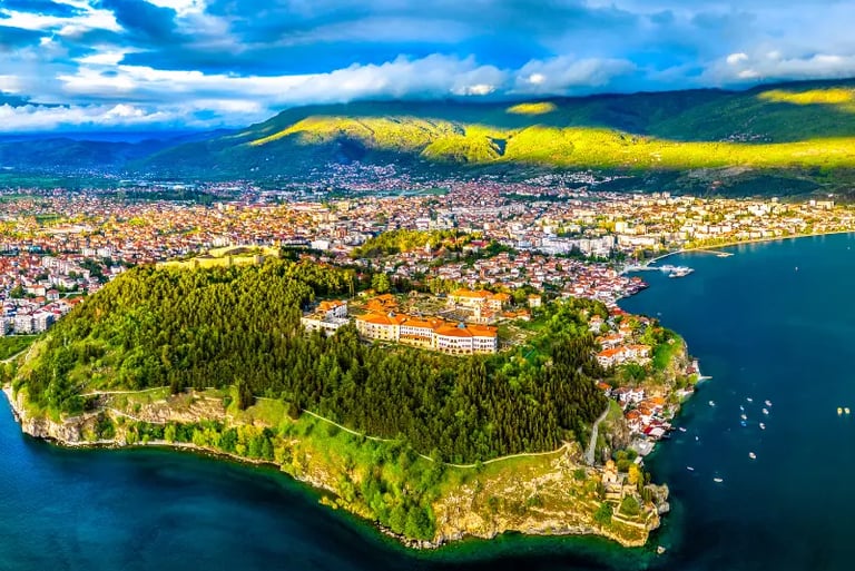 Aerial view of Ohrid city, Samuel's Fortress, and the deep blue Lake Ohrid under a cloudy sky.