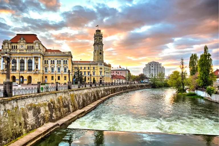 Oradea City Hall and the Crișul Repede river at sunset with colorful clouds over the Romanian architecture.