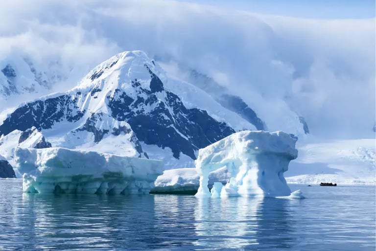 Blue icebergs floating in Antarctic waters with snow-covered mountains and an expedition boat.