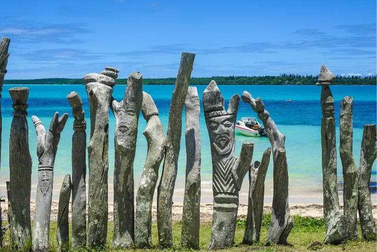 Traditional Kanak wooden totems carved with faces along a tropical turquoise beach in Vanuatu.