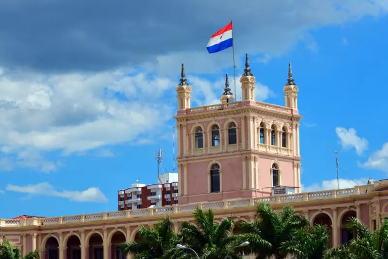 The pink Palacio de los López in Asunción with the Paraguay flag waving under a blue sky.