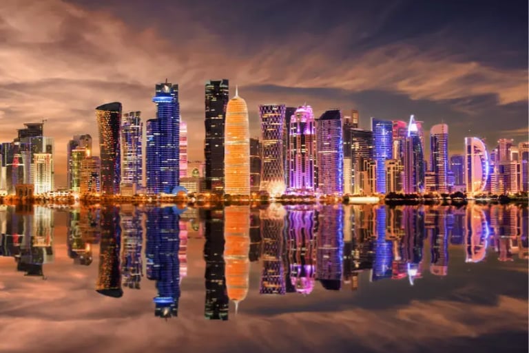 Night skyline of Doha, Qatar with illuminated skyscrapers reflected in the calm water of the bay.