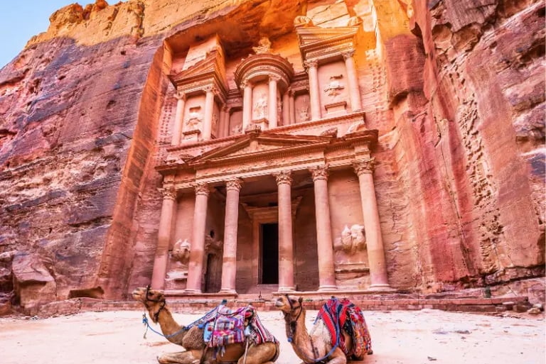 Two camels resting in front of Al-Khazneh temple at the ancient city of Petra in Jordan.