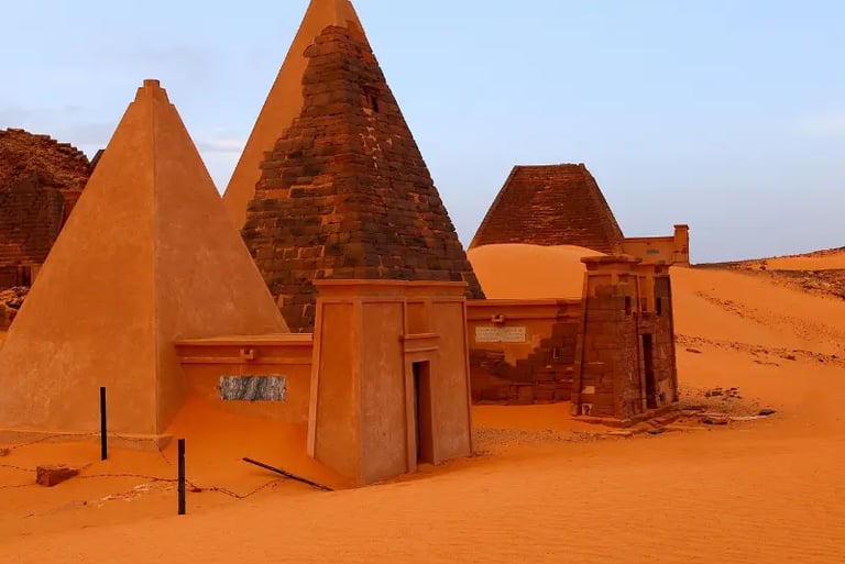 Ancient Nubian pyramids of Meroe in the Sudanese desert with orange sand dunes.
