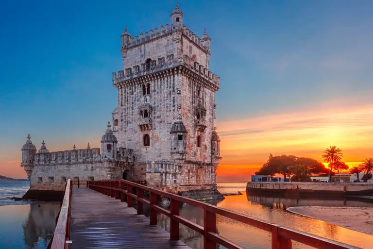The historic Belem Tower in Lisbon at sunset with a wooden walkway over the Tagus River.