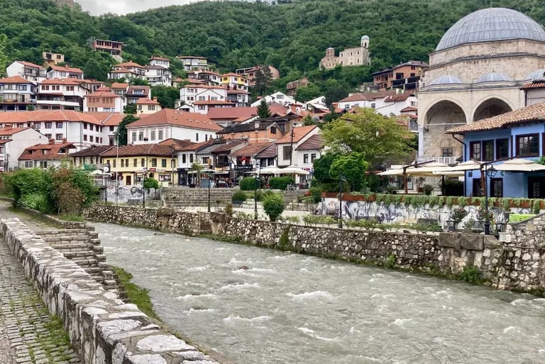 Scenic view of the Bistrica river flowing through Prizren old town with the Sinan Pasha Mosque and historic hillside houses.