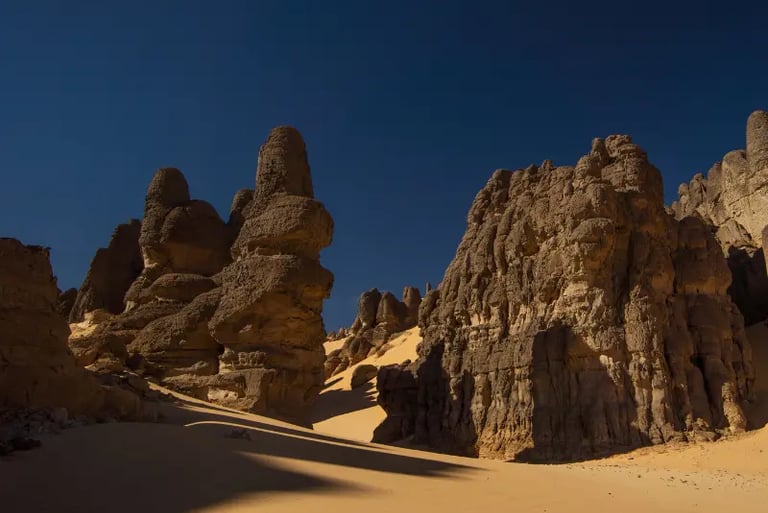 Tall volcanic rock formations and sand dunes under a clear blue sky in the Sahara Desert, Chad