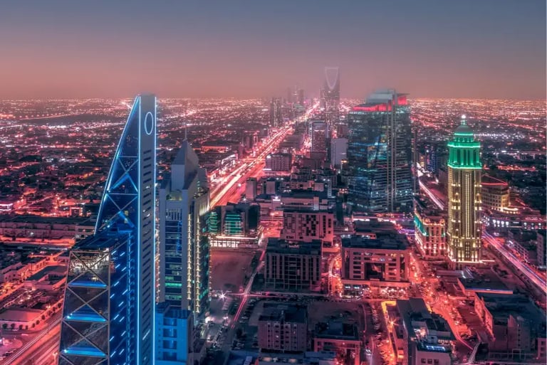 Aerial night view of Riyadh skyline featuring illuminated skyscrapers and city traffic lights in Saudi Arabia.
