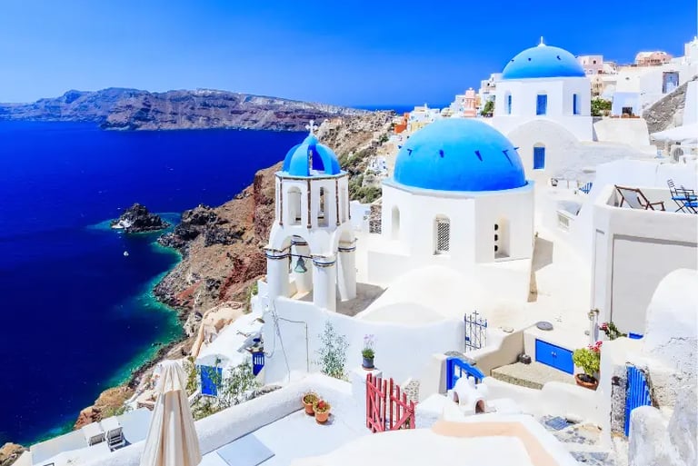 Panoramic view of blue domed churches in Oia, Santorini, overlooking the Aegean Sea.