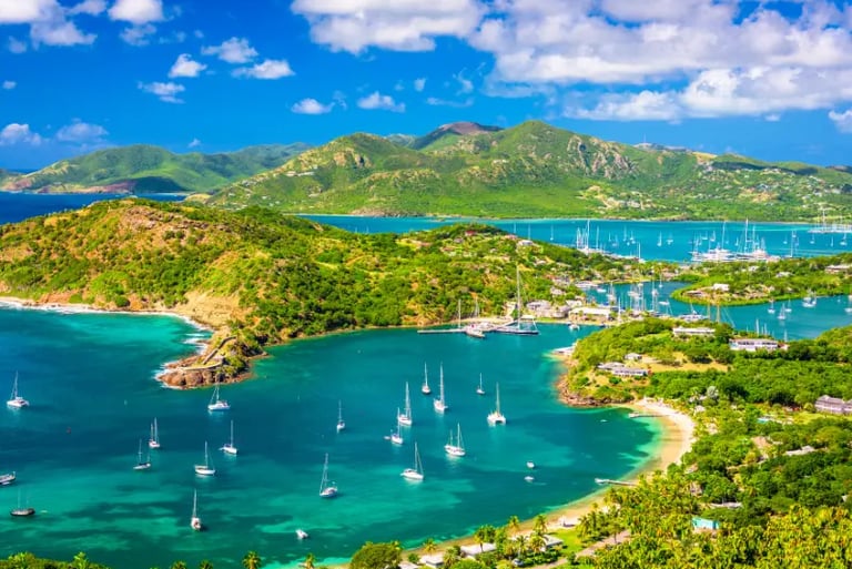 Aerial view of sailboats anchored in the turquoise waters of English Harbour, Antigua, surrounded by lush green hills.
