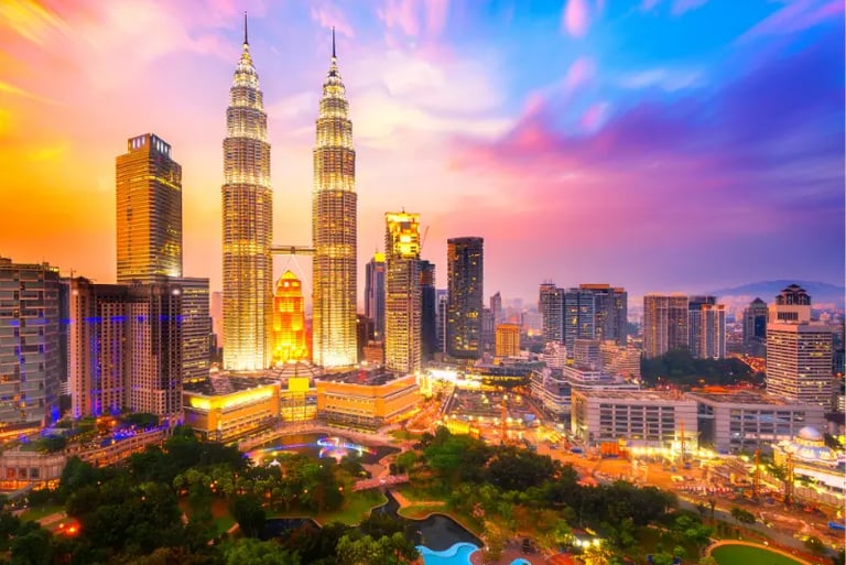 Petronas Twin Towers and Kuala Lumpur city skyline illuminated at sunset with vibrant purple and orange clouds.