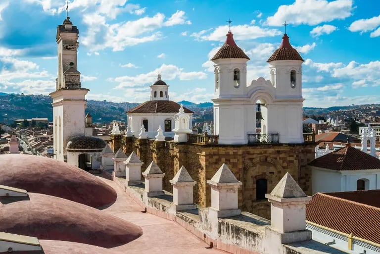 Historic white church towers and rooftop views of Sucre, Bolivia, under a blue sky.