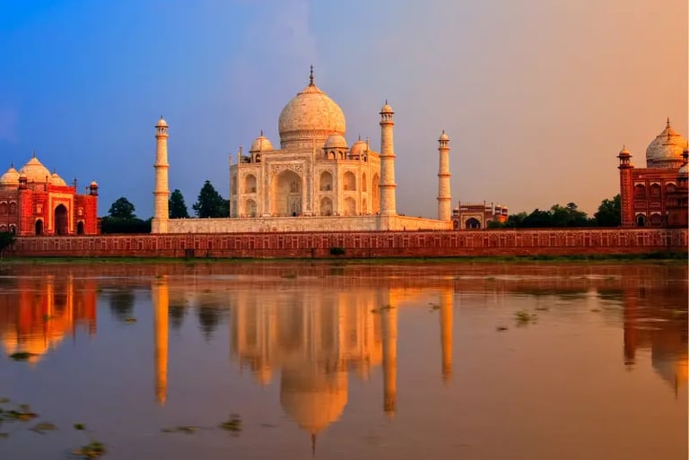The Taj Mahal in Agra reflected in the Yamuna River during a golden hour sunset.
