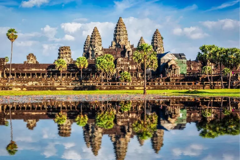 Angkor Wat temple complex in Cambodia reflecting in a lotus pond under a blue sky.