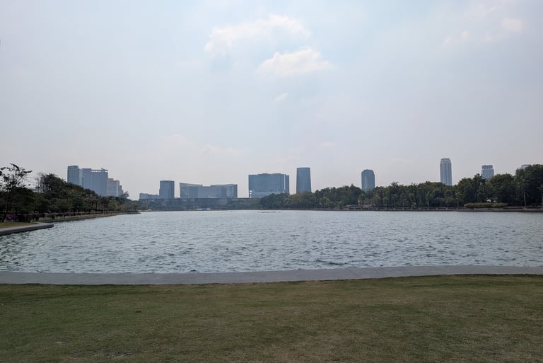 Wide view of Benjakitti Park lake with Bangkok city skyline skyscrapers in the background.