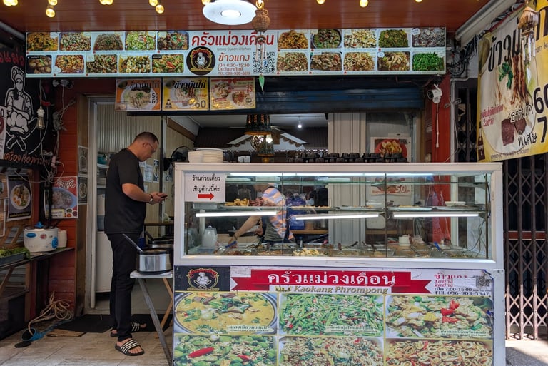 A local Thai street food stall in Bangkok featuring a colorful menu display of traditional curry and stir-fry dishes.