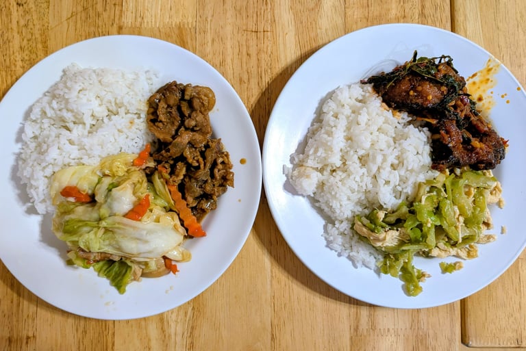 Two plates of Thai food with white rice, stir-fried cabbage, beef, and spicy fish curry on a wooden table.