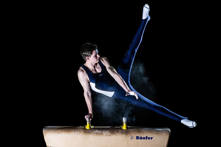 Turner am Pauschenpferd in dynamischer Pose vor schwarzem Hintergrund. Sportfoto von Joel Pingel.