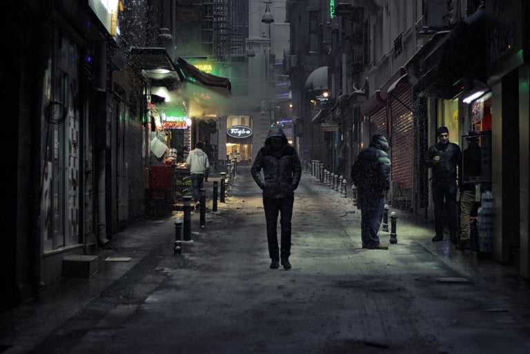 Persona con abrigo caminando por un callejón de noche, transmitiendo soledad e introspección