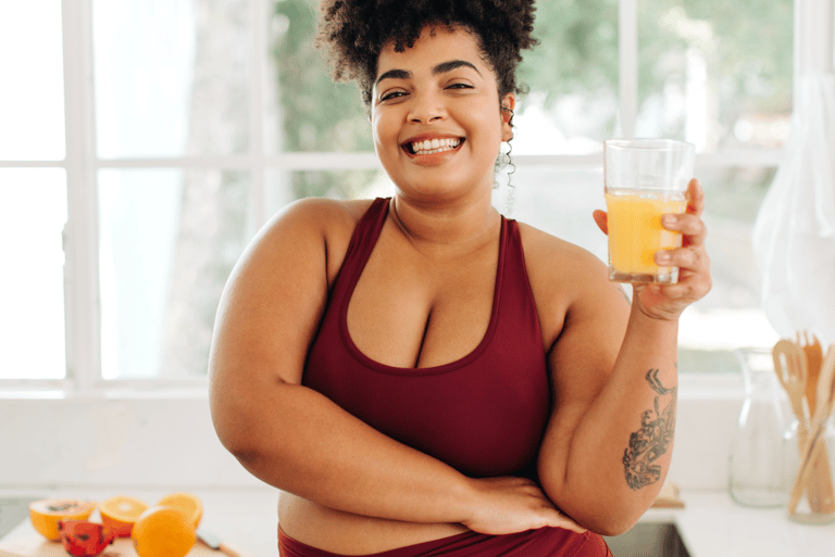 a woman in a red top and yoga pants is holding a glass of orange juice