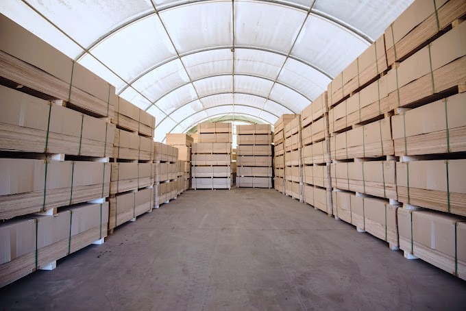 Stacked bundles of plywood sheets in a large industrial warehouse storage facility.