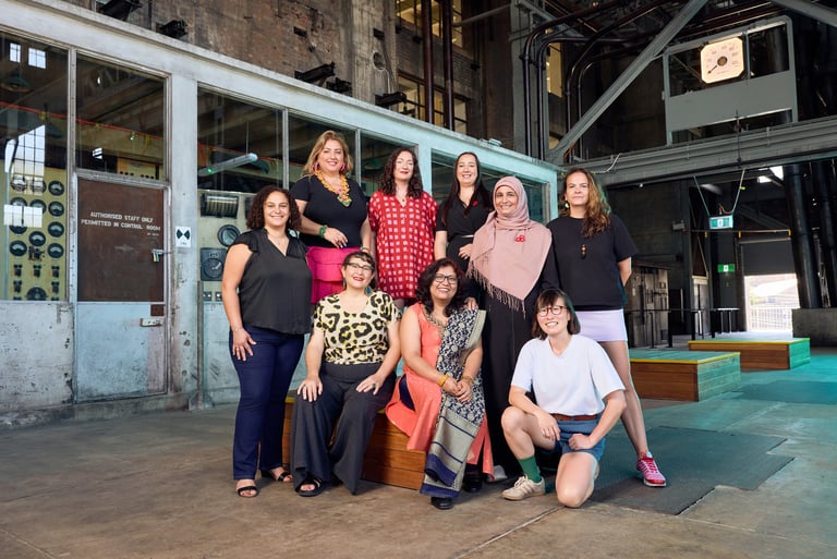 A group of nine people standing, sitting and kneeling in a cavernous industrial space.
