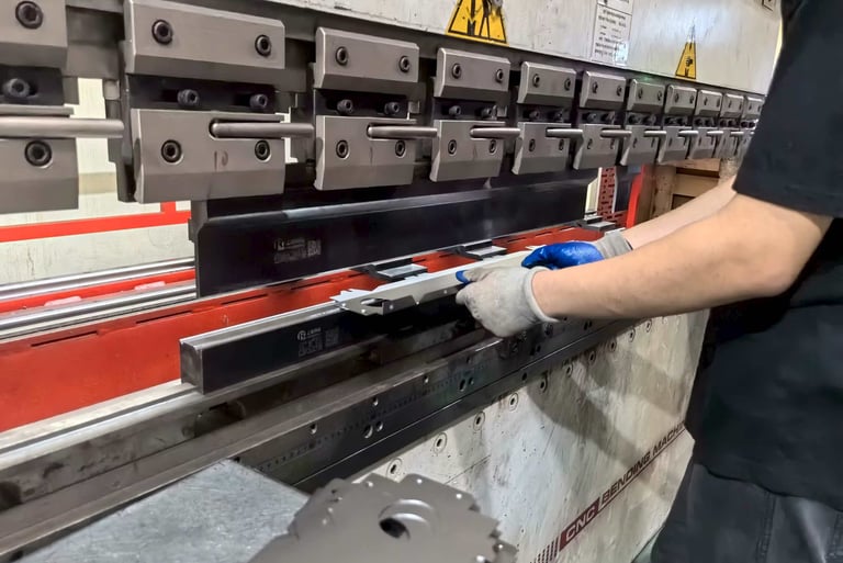 A metal worker uses a hydraulic CNC press brake machine to bend precision sheet metal parts.