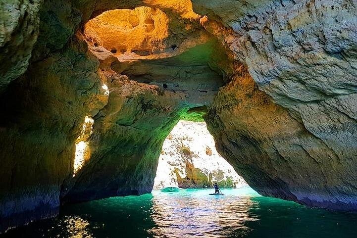 A person paddleboarding through the Benagil sea cave with sunlight streaming through a natural skylight.