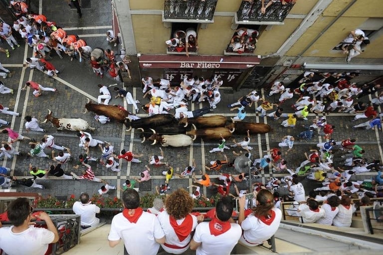 Aerial view of bulls and participants running through cobblestone streets during the San Fermin festival in Pamplona.