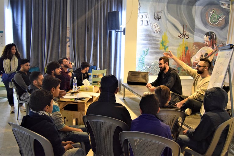 a group of people sitting around a table attending a workshop on rap music composition