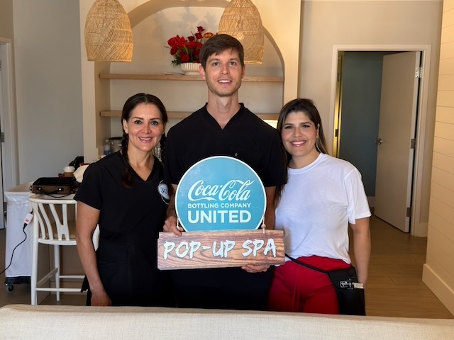 Three spa professionals posing with a Coca-Cola Bottling Company United pop-up spa sign.