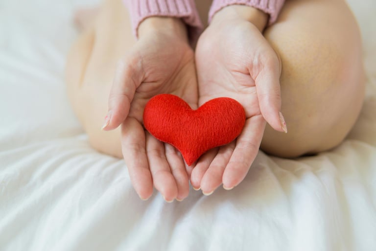 a felt heart being held in a person's hands while they are kneeling on a bed