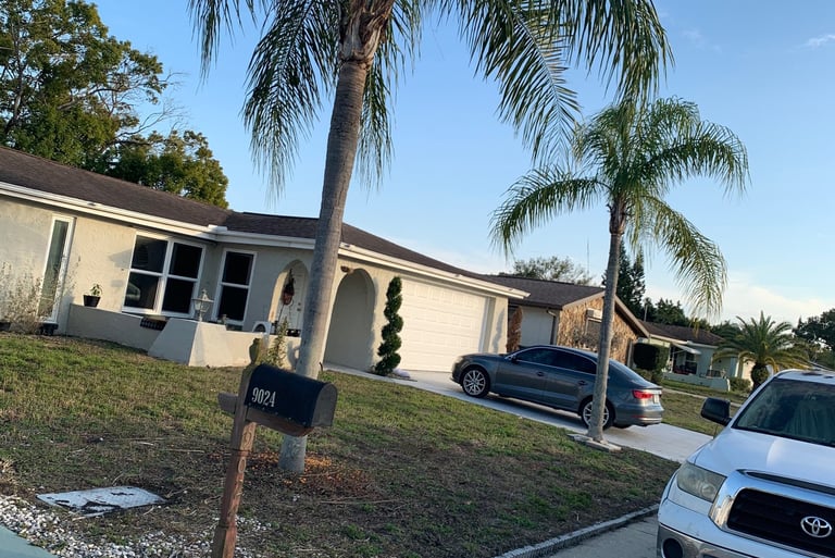 A Florida suburban home with palm trees, a green lawn, and parked cars under a blue sky.