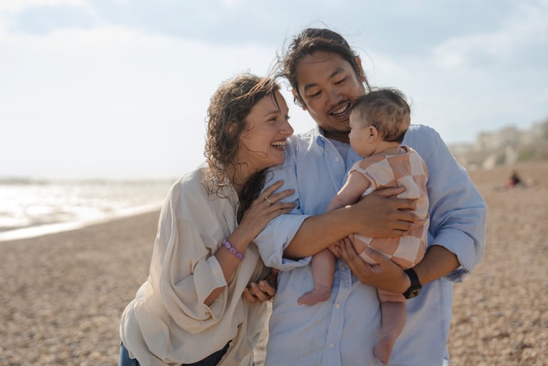 Family of three laughing on the beach with baby on the arms